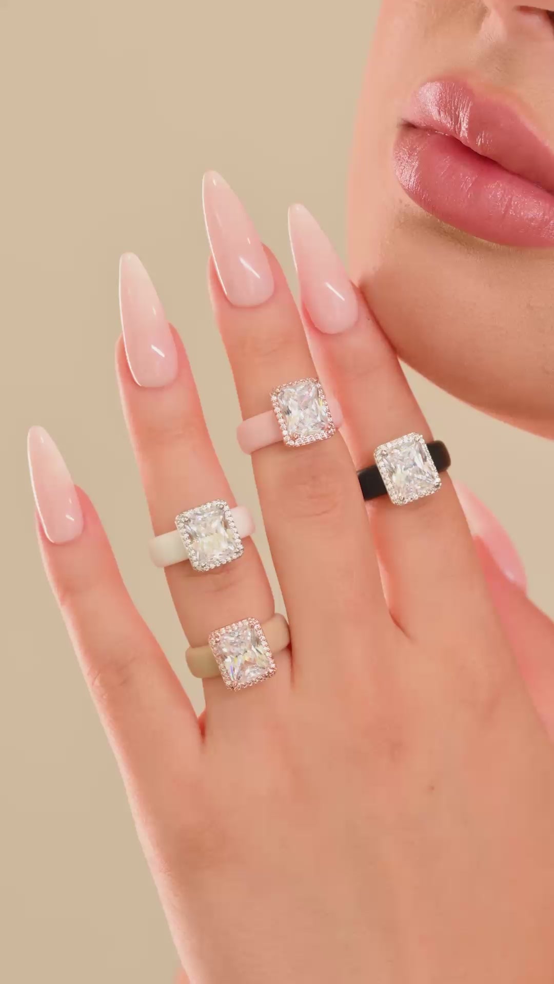 Hand wearing silicone rings with emerald-cut clear halo stones in several colors