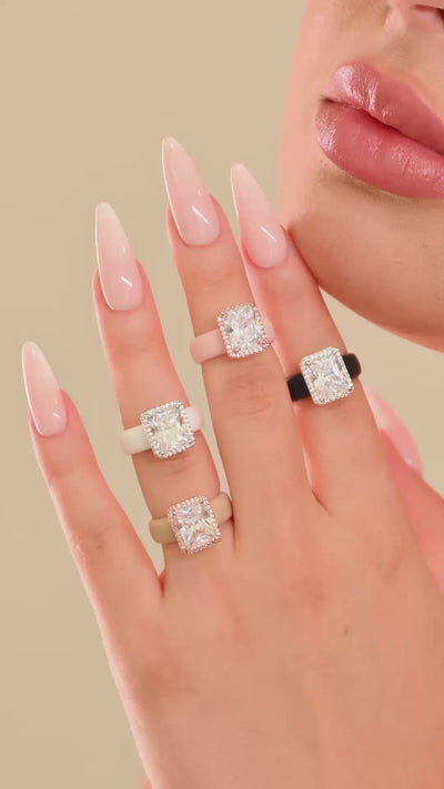 Hand wearing silicone rings with emerald-cut clear halo stones in several colors